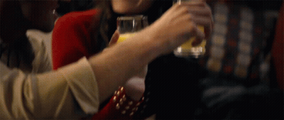 A Woman Is Holding A Glass Of Orange Juice In Her Hand GIF