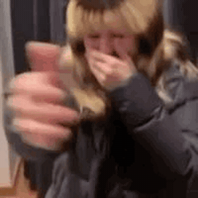 A Woman Is Holding A Glass Of Wine And Covering Her Mouth With Her Hand . GIF