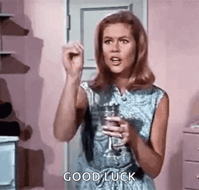 A Woman Is Holding A Glass Of Wine And Giving A Good Luck Sign . GIF