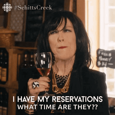 A Woman Is Holding A Glass Of Wine And Says I Have My Reservations What Time Are They GIF