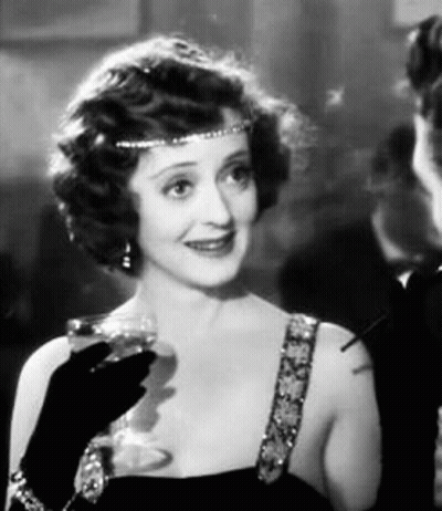 A Woman Is Holding A Glass Of Wine And Smoking A Cigarette . GIF