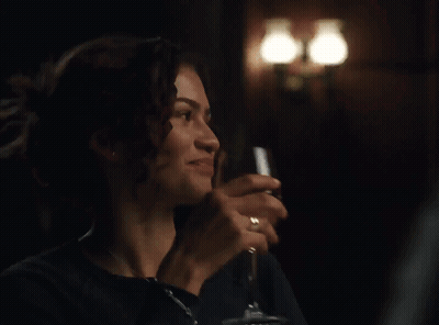 A Woman Is Holding A Glass Of Wine In A Dark Room GIF