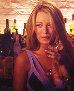 A Woman Is Holding A Glass Of Wine In Front Of A Bar GIF