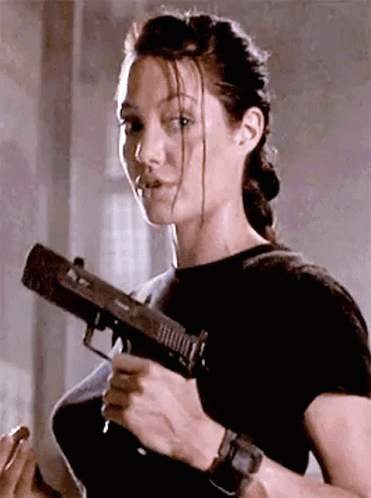 A Woman Is Holding A Gun In Her Hand And Looking At The Camera . GIF