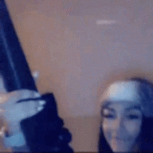 A Woman Is Holding A Gun In Her Hand And Smiling . GIF