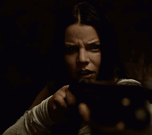 A Woman Is Holding A Gun In Her Hand In A Dark Room And Pointing At The Camera . GIF
