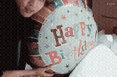 A Woman Is Holding A Happy Birthday Balloon In Her Hands . GIF