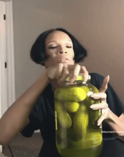 A Woman Is Holding A Jar Of Pickles In Her Hands . GIF