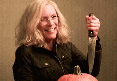 A Woman Is Holding A Knife Over A Pumpkin And Smiling . GIF