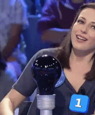 A Woman Is Holding A Light Bulb And Wearing A Number 1 Badge GIF