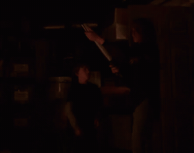 A Woman Is Holding A Light While Standing Next To A Boy In A Blue Shirt GIF