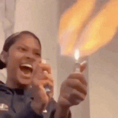 A Woman Is Holding A Lighter With A Flame Coming Out Of It And Laughing . GIF