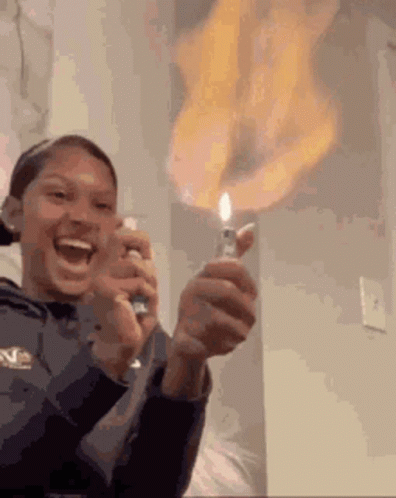 A Woman Is Holding A Lighter With Flames Coming Out Of It And Smiling . GIF