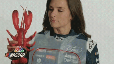 A Woman Is Holding A Lobster In Front Of A Nascar Sign GIF