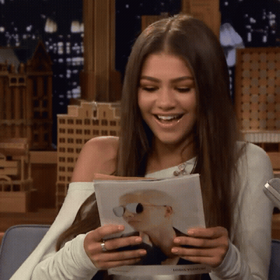 A Woman Is Holding A Magazine That Says Louis Vuitton On It GIF