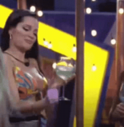 A Woman Is Holding A Martini Glass In Front Of A Yellow And Blue Wall . GIF