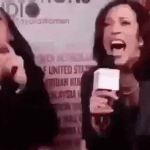 A Woman Is Holding A Microphone And Screaming Into It While Another Woman Looks On . GIF