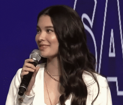 A Woman Is Holding A Microphone And Smiling While Standing In Front Of A Purple Background . GIF