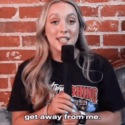 A Woman Is Holding A Microphone In Front Of A Brick Wall And Saying Get Away From Me . GIF