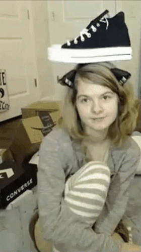 A Woman Is Holding A Pair Of Black Converse Shoes On Her Head . GIF