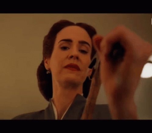 A Woman Is Holding A Pair Of Scissors And Looking At The Camera . GIF