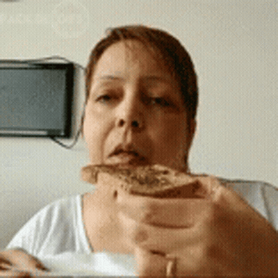 A Woman Is Holding A Piece Of Bread In Front Of Her Face . GIF