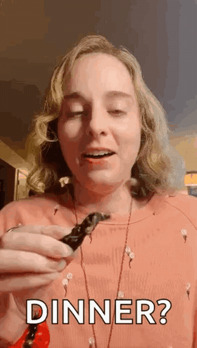 A Woman Is Holding A Piece Of Food In Her Hand And Saying `` Dinner ? '' . GIF