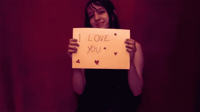 A Woman Is Holding A Piece Of Paper That Says I Love You GIF