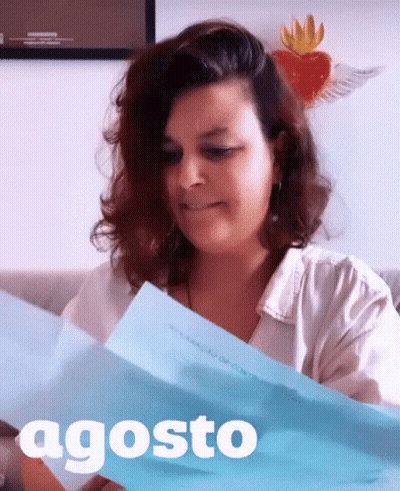A Woman Is Holding A Piece Of Paper With The Word Agosto On It GIF