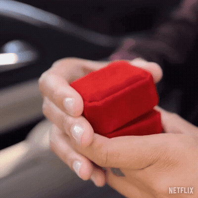 A Woman Is Holding A Red Box With A Ring Inside Of It . GIF