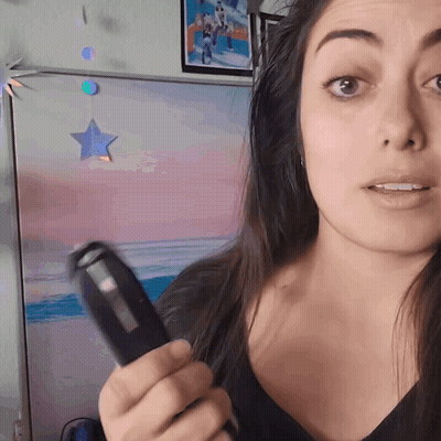 A Woman Is Holding A Remote Control In Front Of A Painting Of A Beach GIF