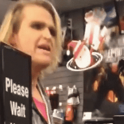 A Woman Is Holding A Sign That Says " Please Wait " GIF