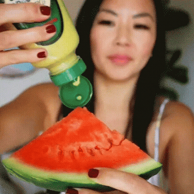 A Woman Is Holding A Slice Of Watermelon With A Bottle Of Mustard On It GIF