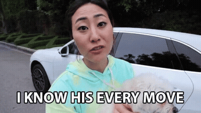 A Woman Is Holding A Small White Dog In Front Of A White Car And Says I Know His Every Move GIF