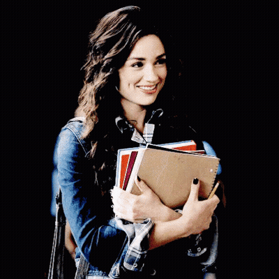 A Woman Is Holding A Stack Of Books And Smiling GIF
