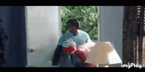 A Woman Is Holding A Stuffed Animal And A Lamp While Standing In Front Of A Doorway . GIF