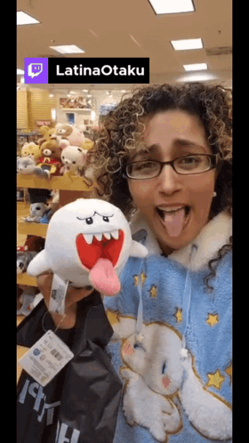 A Woman Is Holding A Stuffed Animal In Front Of A Sign That Reads Latinaotaku GIF