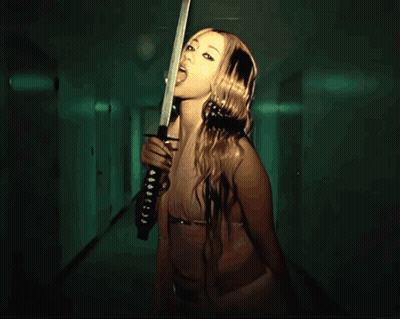 A Woman Is Holding A Sword In A Hallway With A Green Light Behind Her GIF
