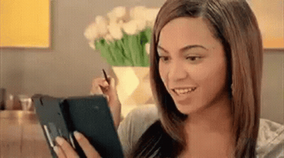 A Woman Is Holding A Tablet In Her Hand And Smiling . GIF
