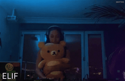 A Woman Is Holding A Teddy Bear In Front Of A Sign That Says Elif GIF