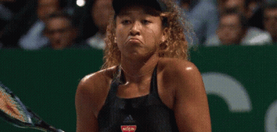 A Woman Is Holding A Tennis Racquet And Making A Funny Face While Playing Tennis . GIF