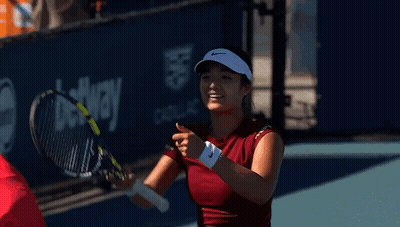 A Woman Is Holding A Tennis Racquet And Smiling . GIF