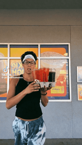 A Woman Is Holding A Tray Of Food In Front Of A Window With A Sign That Says ' Ok Hot ' On It GIF