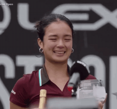 A Woman Is Holding A Trophy And A Bottle Of Champagne In Front Of A Sign That Says Plex Open GIF