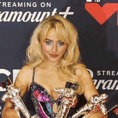 A Woman Is Holding A Trophy In Front Of A Banner That Says Streaming On Amour + GIF
