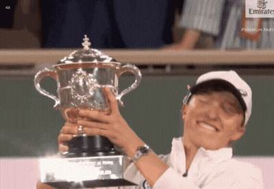 A Woman Is Holding A Trophy In Front Of A Emirates Sign GIF