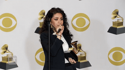 A Woman Is Holding A Trophy In Front Of A Wall With Cbs Logos GIF