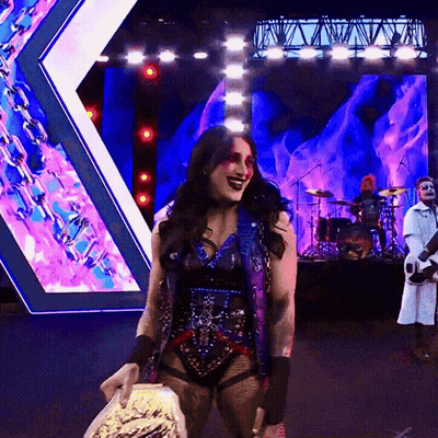 A Woman Is Holding A Trophy On A Stage With A Band Behind Her GIF