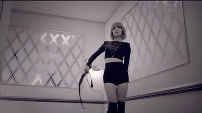 A Woman Is Holding A Whip In Front Of A Wall With The Letters Xx On It GIF
