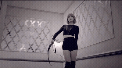 A Woman Is Holding A Whip In Front Of A Wall With The Letters Xx On It GIF